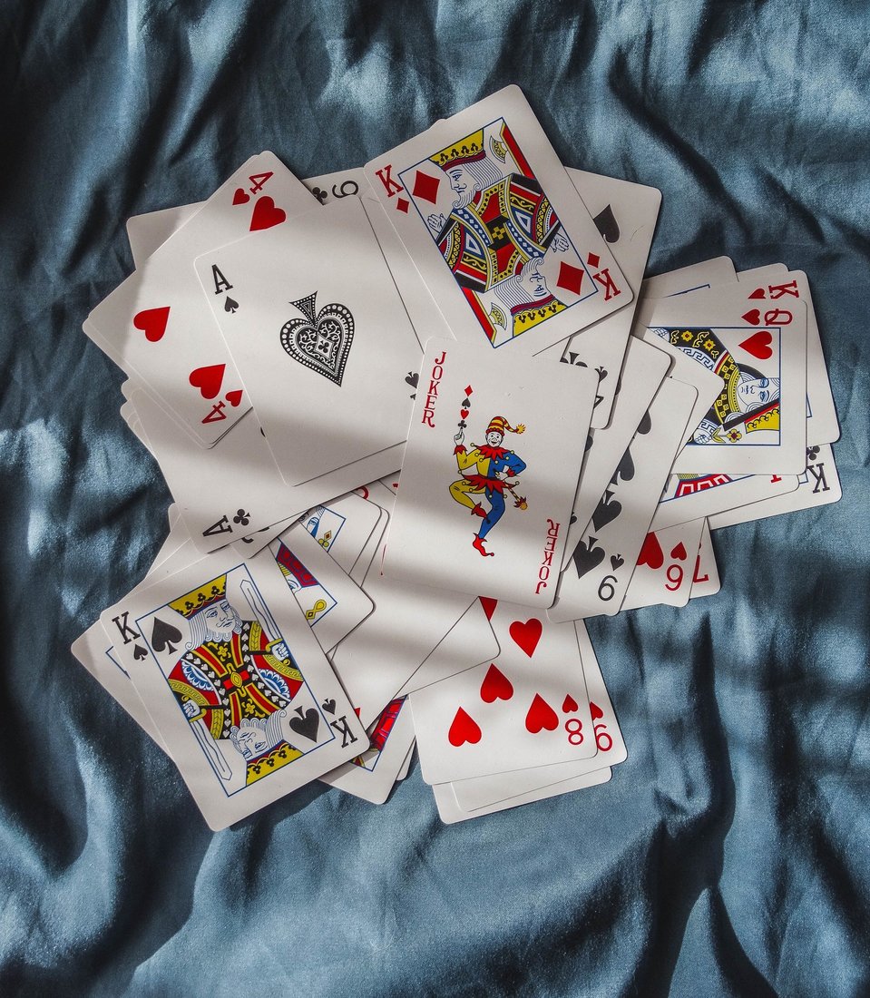 A scattered deck of playing cards face up on a blue cloth, a joker near the centre