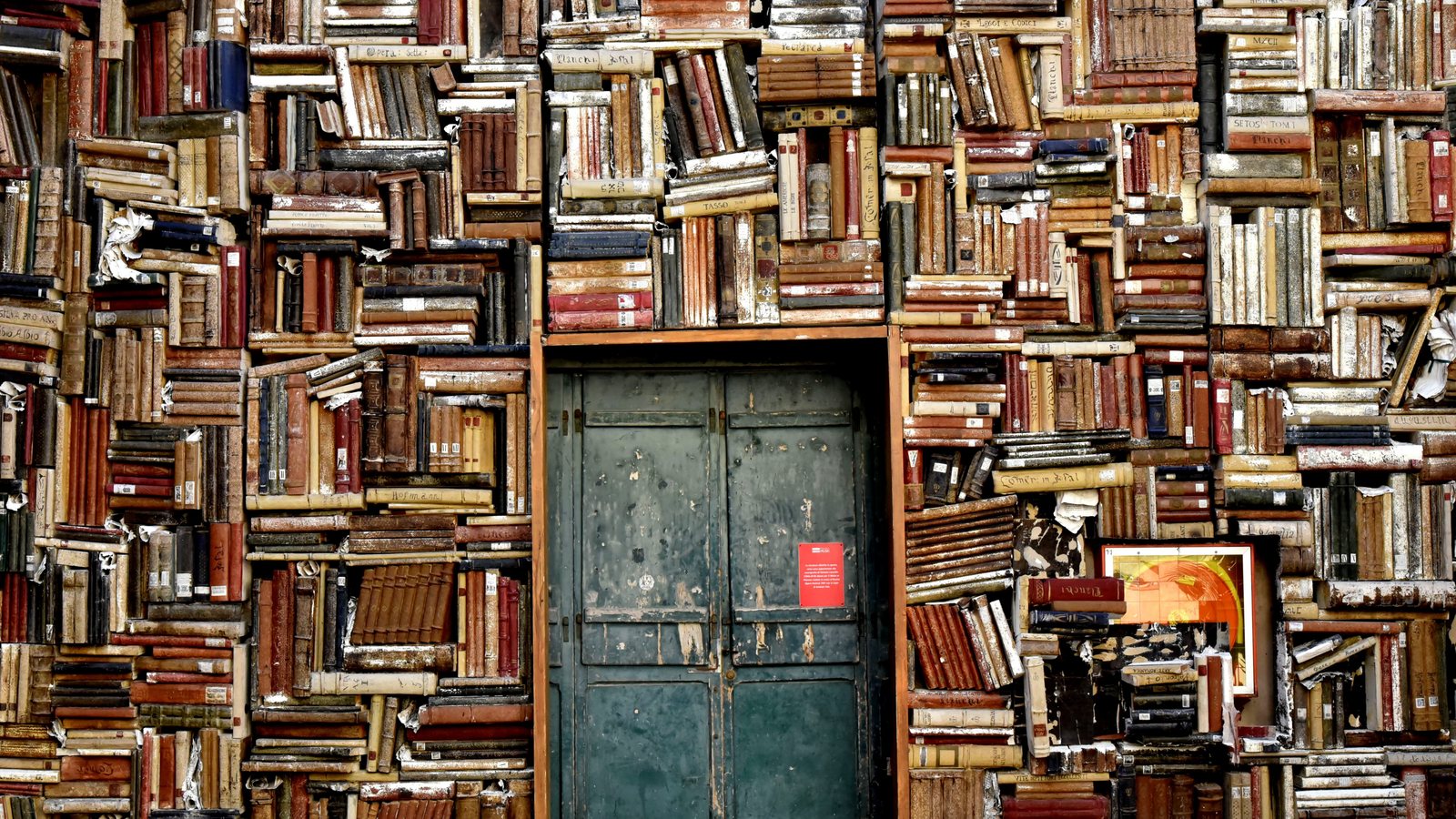 A wall built entirely of old books surrounding a weathered green door