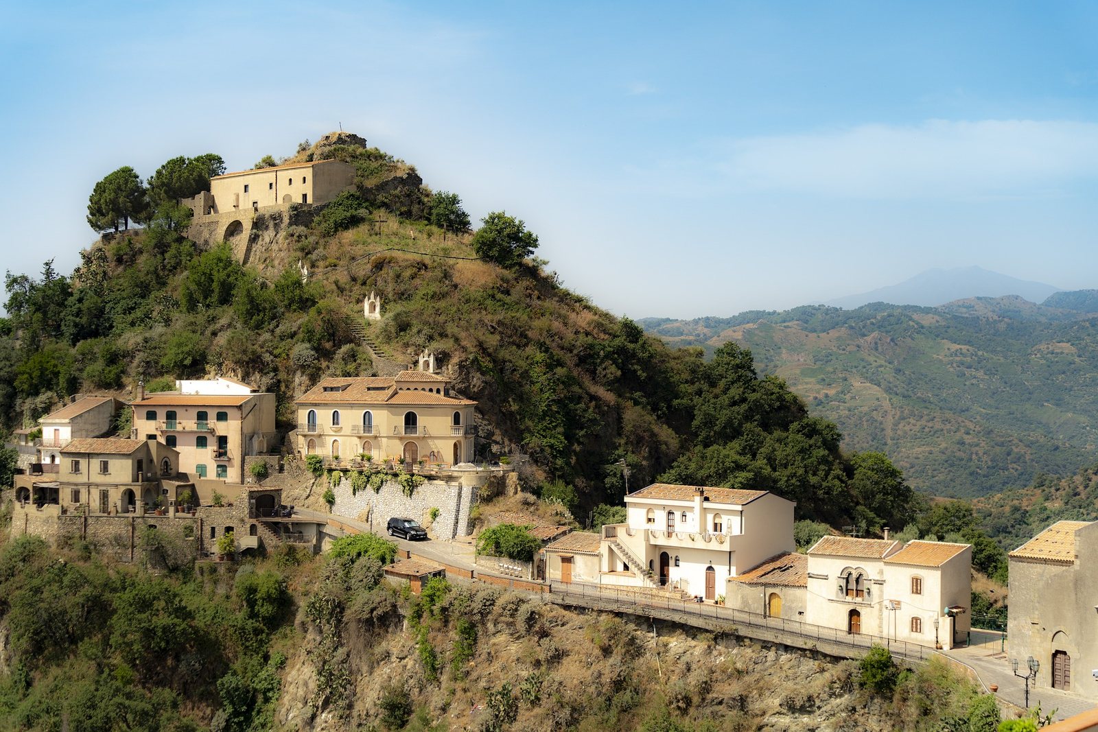 A hilltop village in Sicily, pale houses stacked along the ridge with hazy mountains beyond