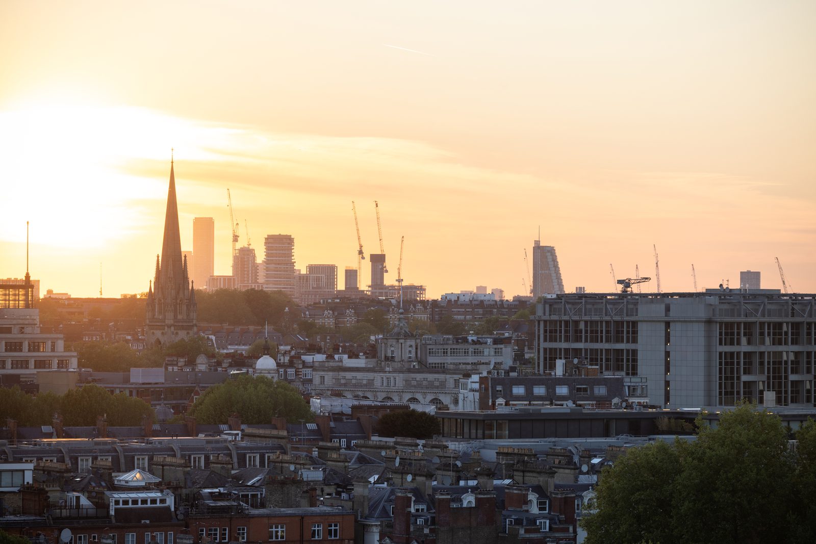 West London rooftops at sunset, a church spire in silhouette and the city skyline beyond