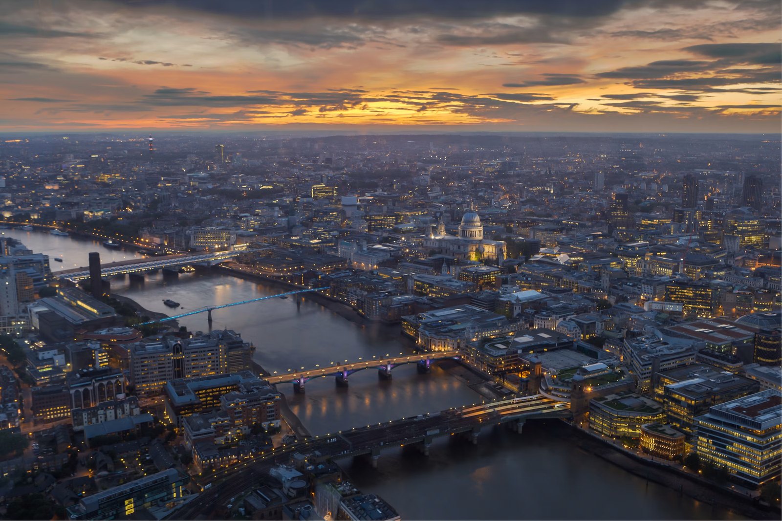 London at dusk from above: the Thames, its bridges lit, and St Paul's against a sunset sky