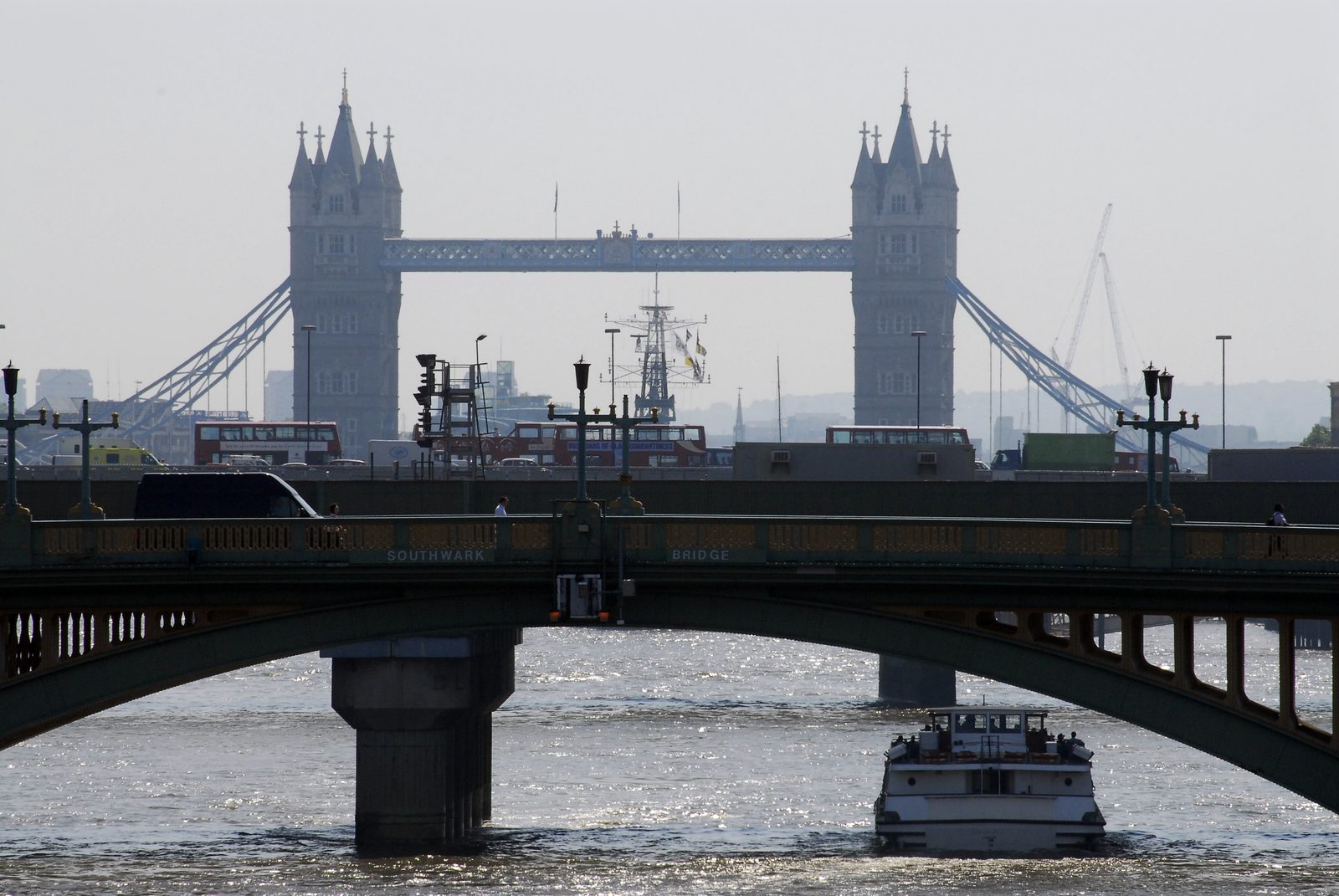 Tower Bridge seen down the Thames through summer haze, a riverboat passing under Southwark Bridge in the foreground